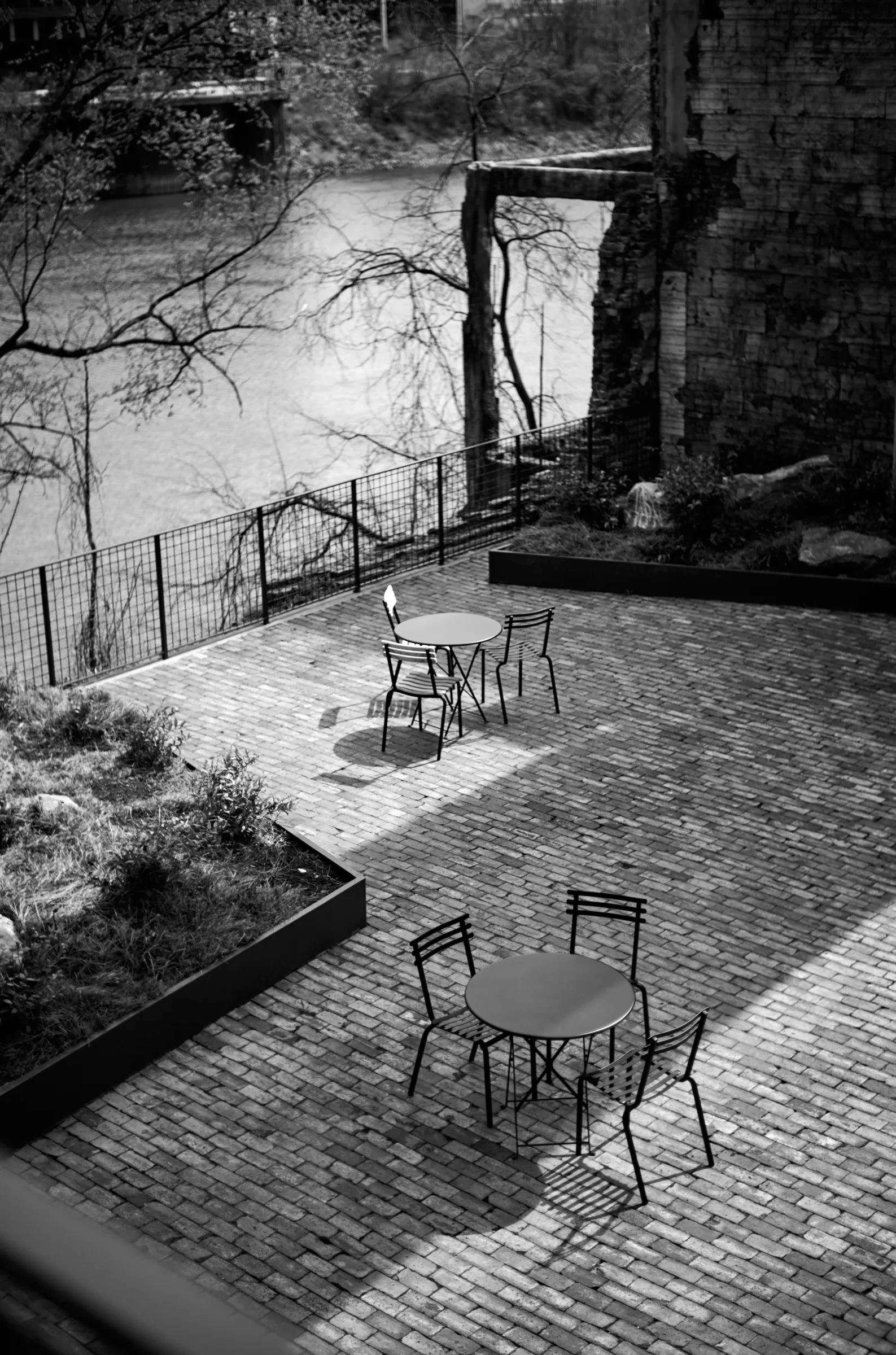 Empty café tables on a brick patio, overlooking a river and a ruined brick wall, Germantown