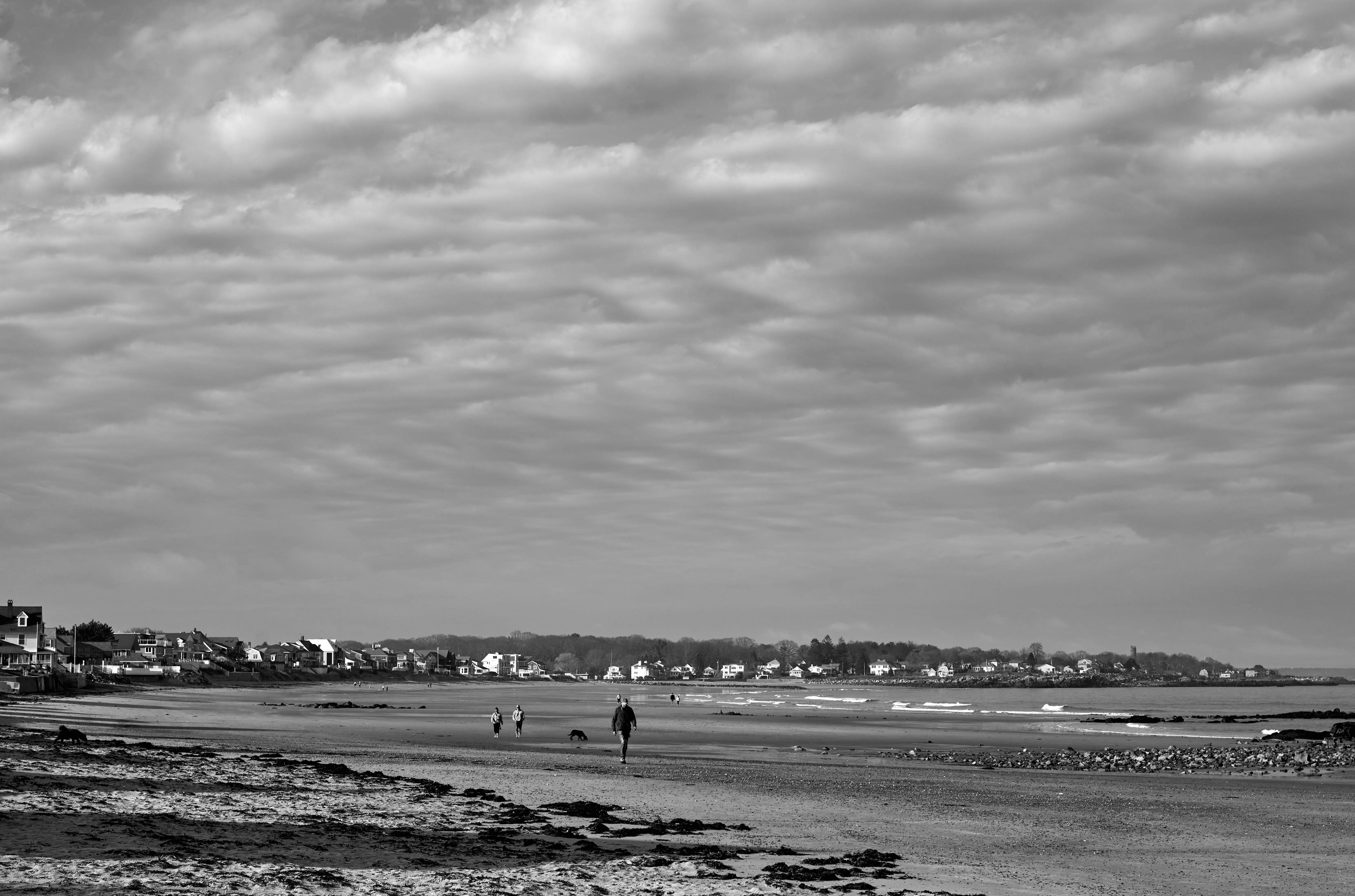Dramatic cloudscape over a wide beach, three walkers and a dog in the middle distance